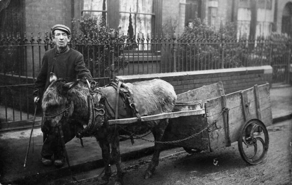 Postcard image of Billy Wright with his homemade cart, with its mangle wheels and his donkey.